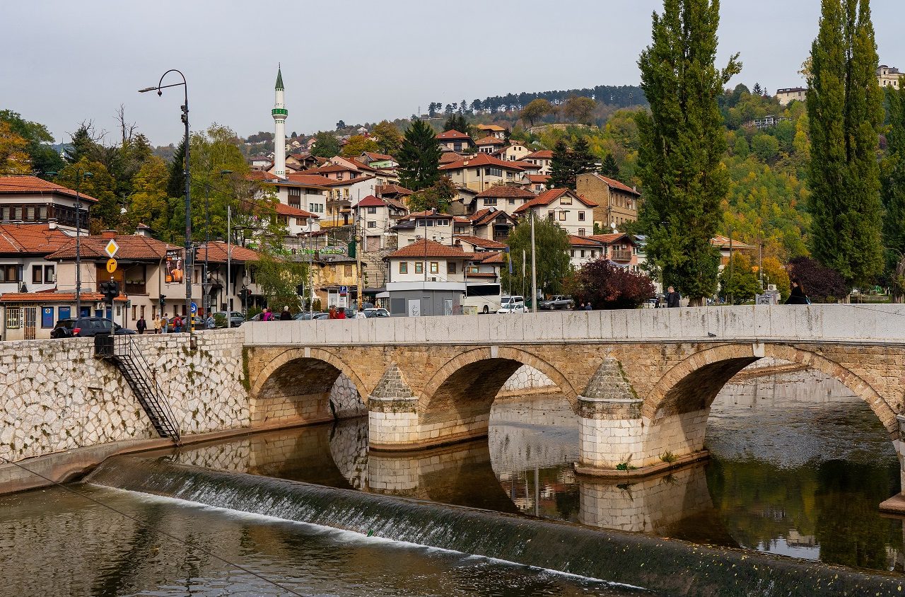 Rivier-met-brug-en-uitzicht-op-woonwijk-in-Sarajevo